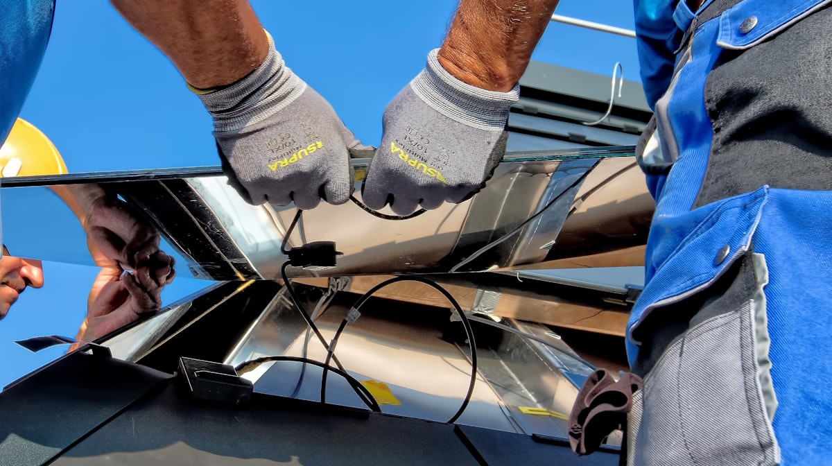Solar installer fitting panel cabling on a rooftop, gloves and PPE visible