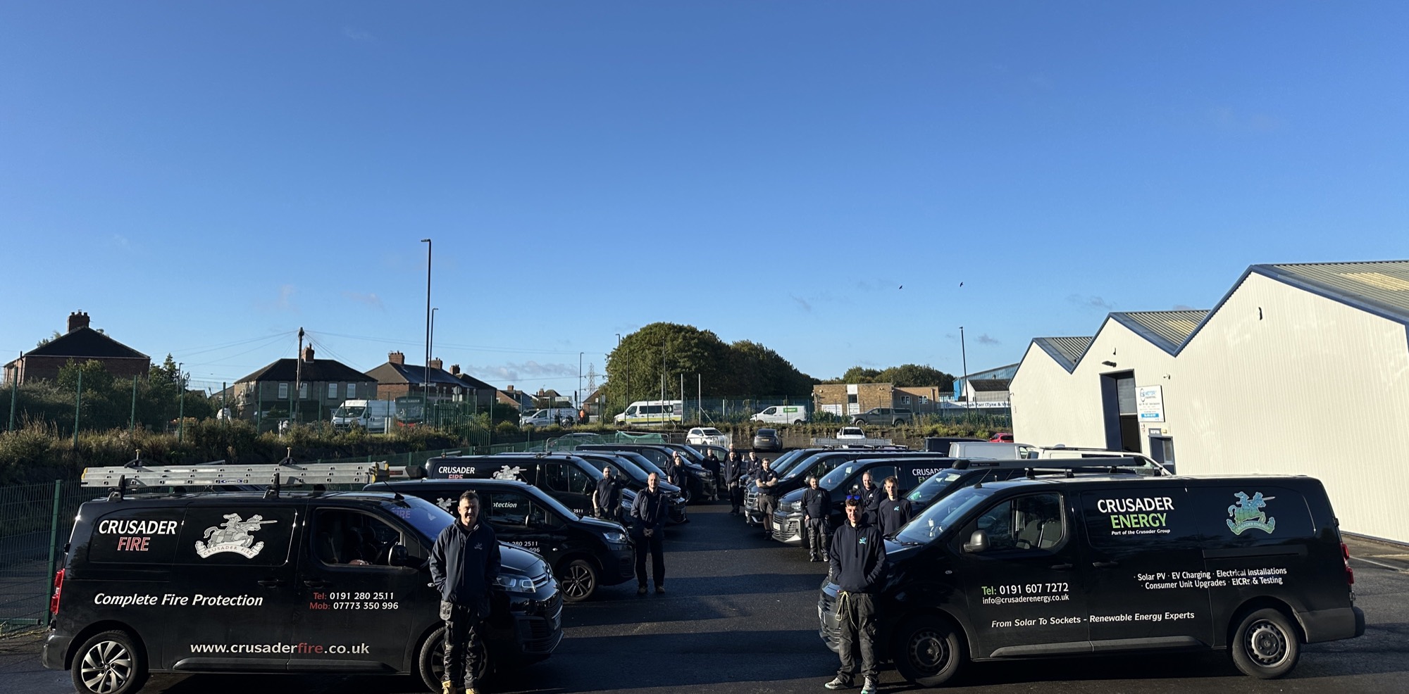 The Crusader Energy team in front of their fleet of black branded vans at St Mary's Lighthouse, Whitley Bay